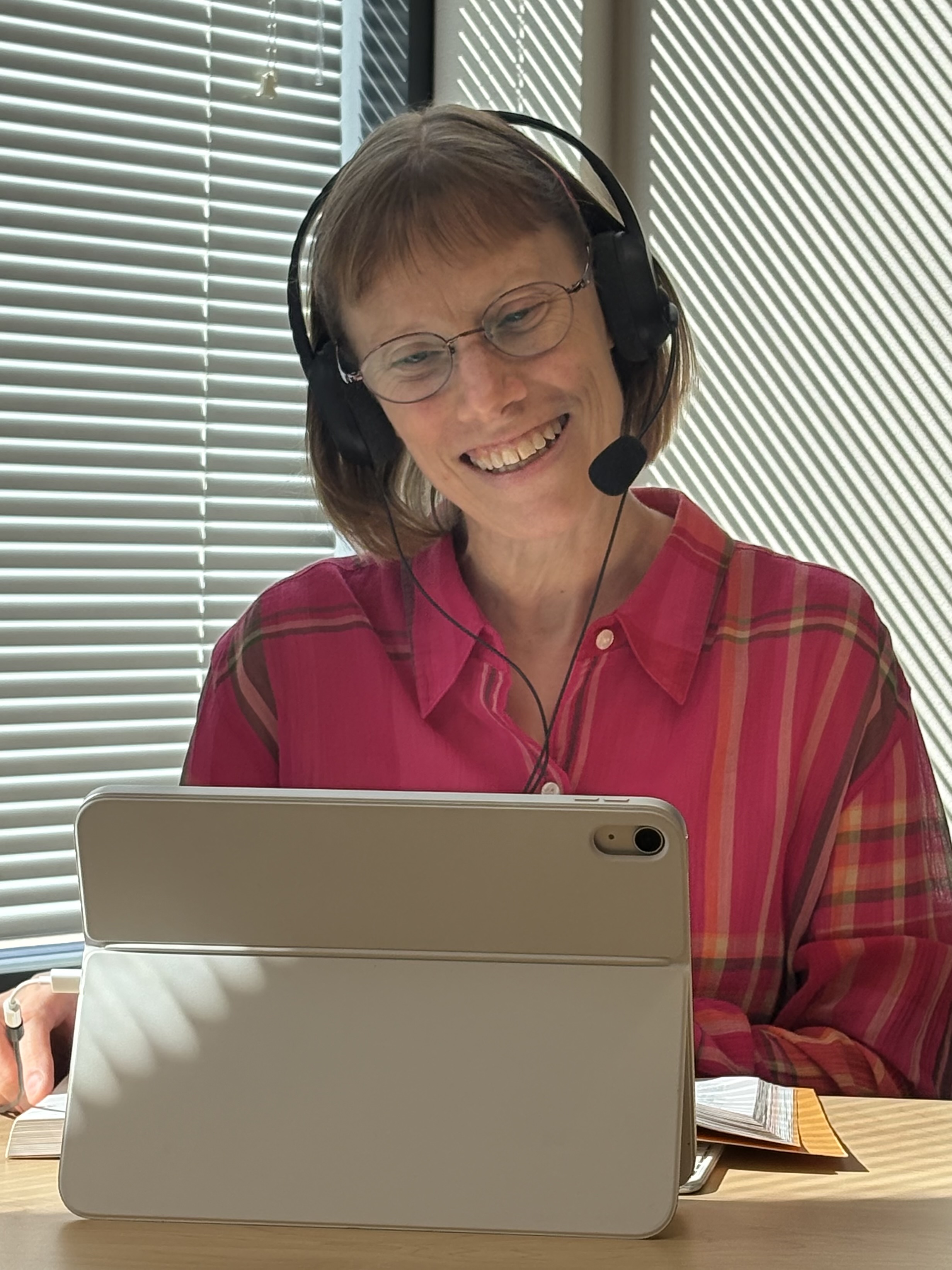 Cory smiling at her iPad while wearing a headset and sitting at her desk.