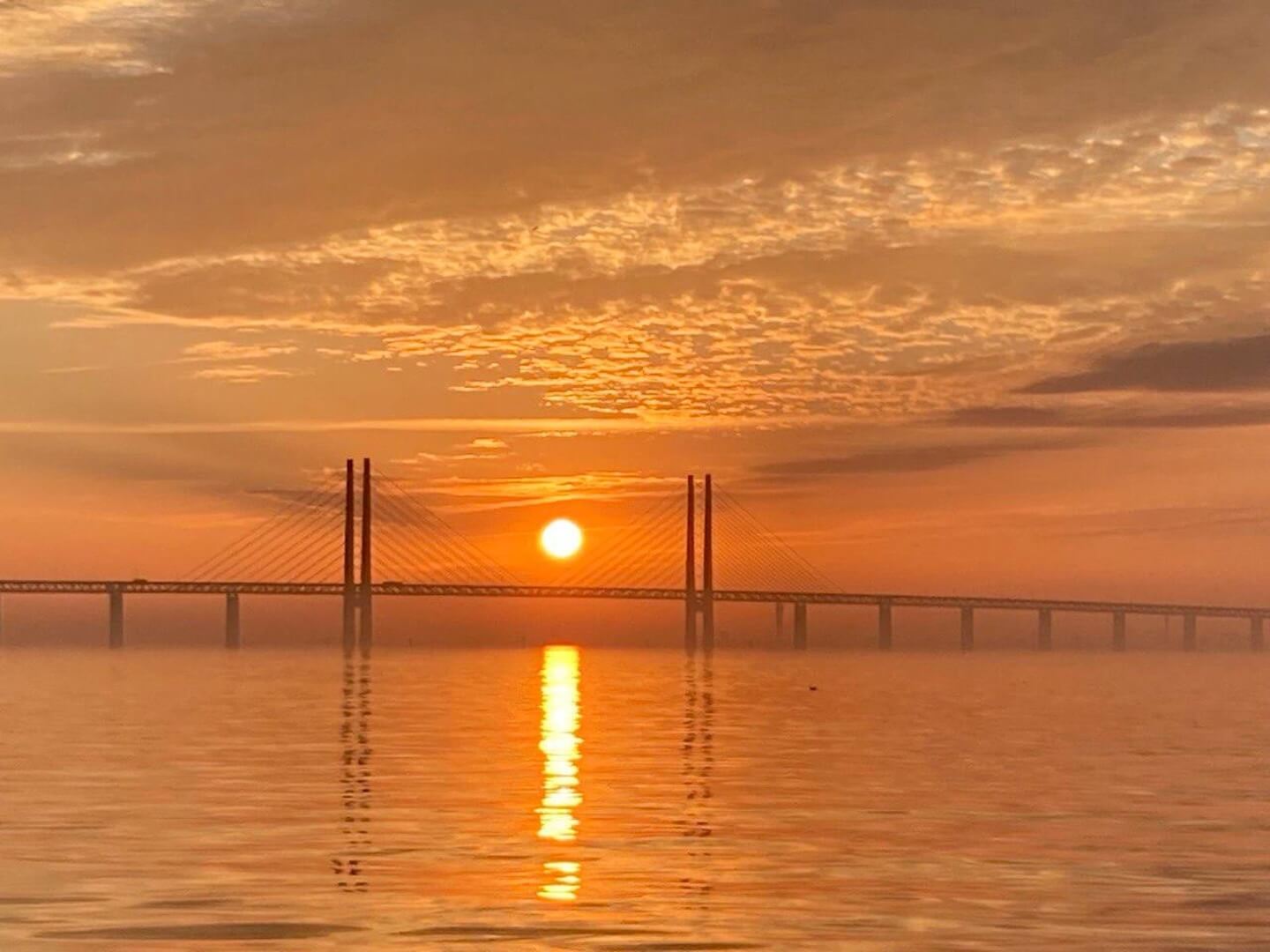 Zonsopgang boven de Sont met de Øresundbrug als silhouet, gefotografeerd vanaf het water tijdens de doortocht naar Denemarken.