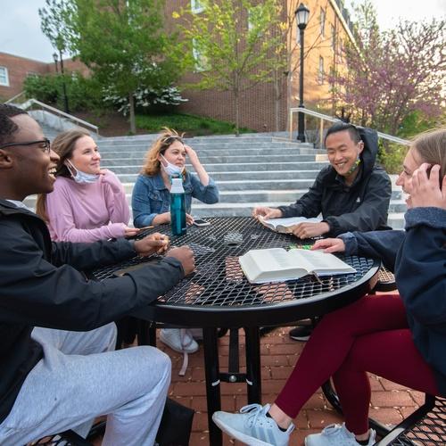 College students reading the Bible while sitting outside at a table.