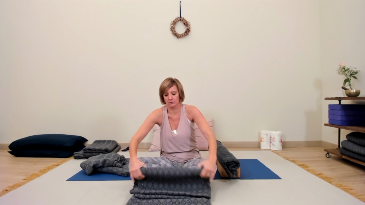 Fotogramma del video Salamba Savasana del Modulo 1: Audrey Favreau, seduta sul tappetino, arrotola una coperta