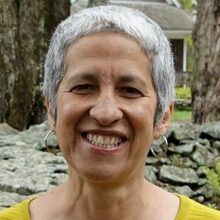 Portrait of teacher Bruni Davila in front of a gray stone wall.