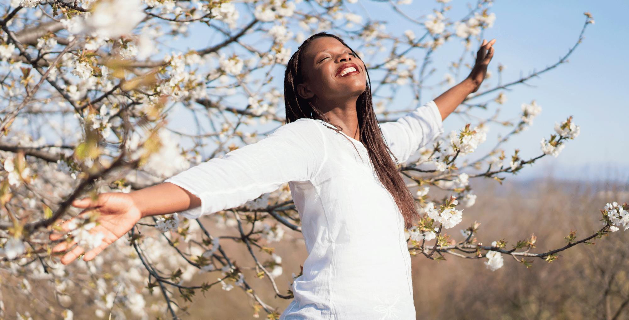 A person with her arms outstretched in front of a treeDescription automatically generated