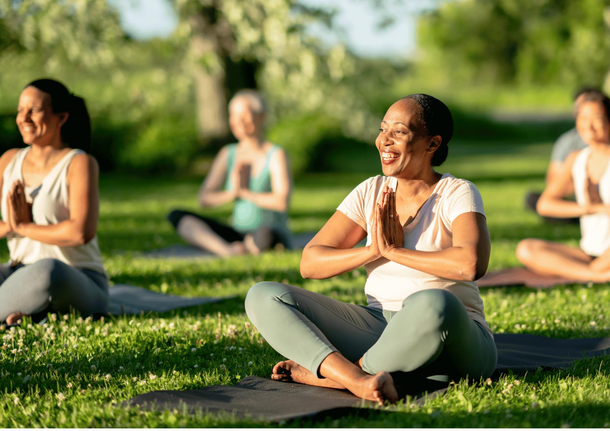 A group of people sitting on yoga mats in the grassDescription automatically generated
