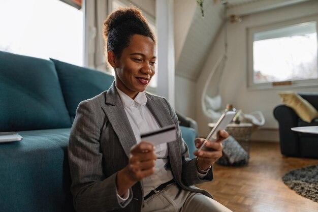 Photo happy black businesswoman using smart phone and shopping online with credit card while working at home