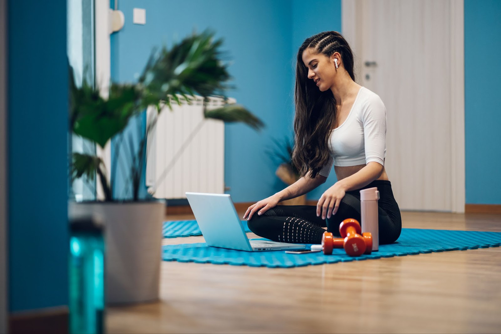Woman sitting on a blue yoga mat using a laptop computer
