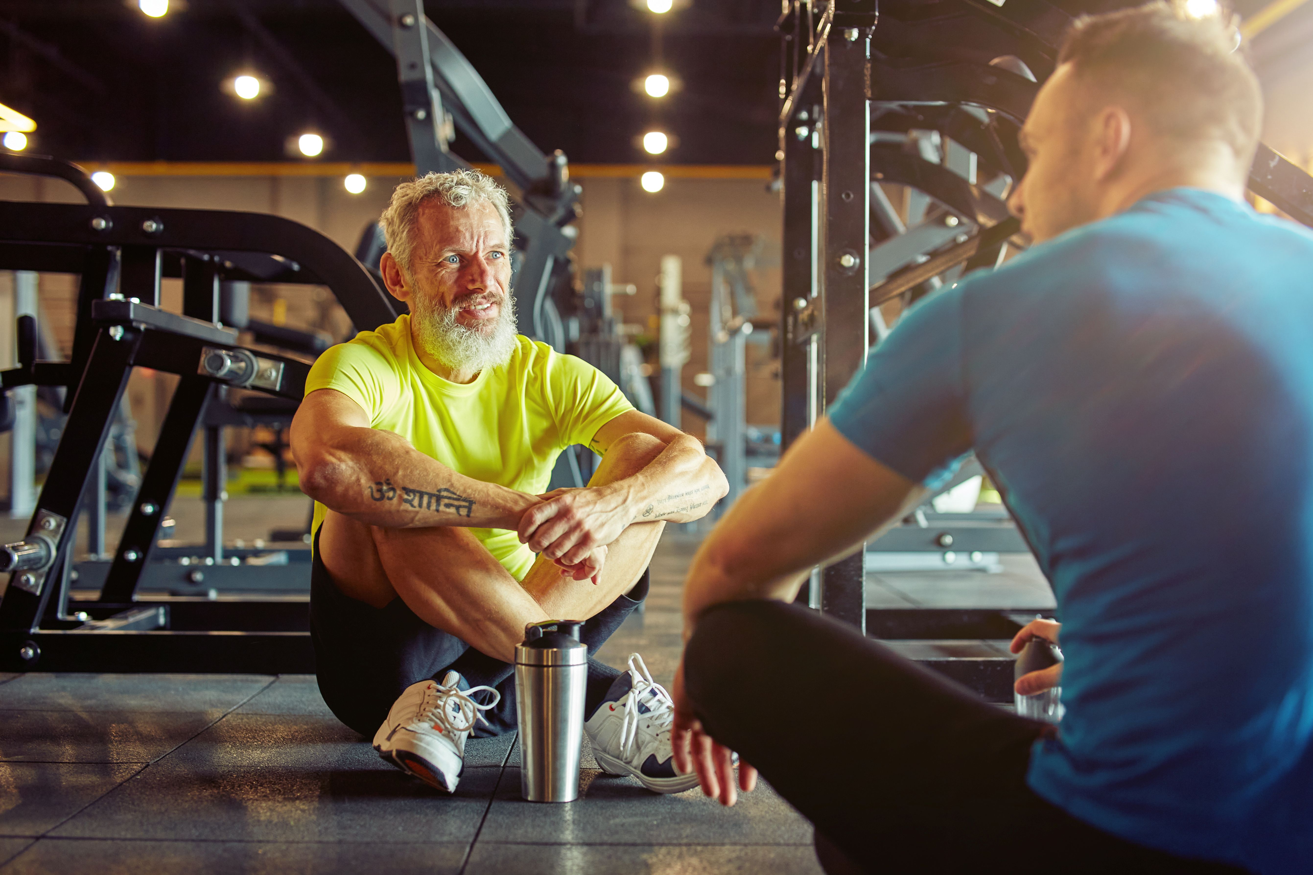 Athletic middle aged man discussing something with personal trainer while sitting together on the floor a gym
