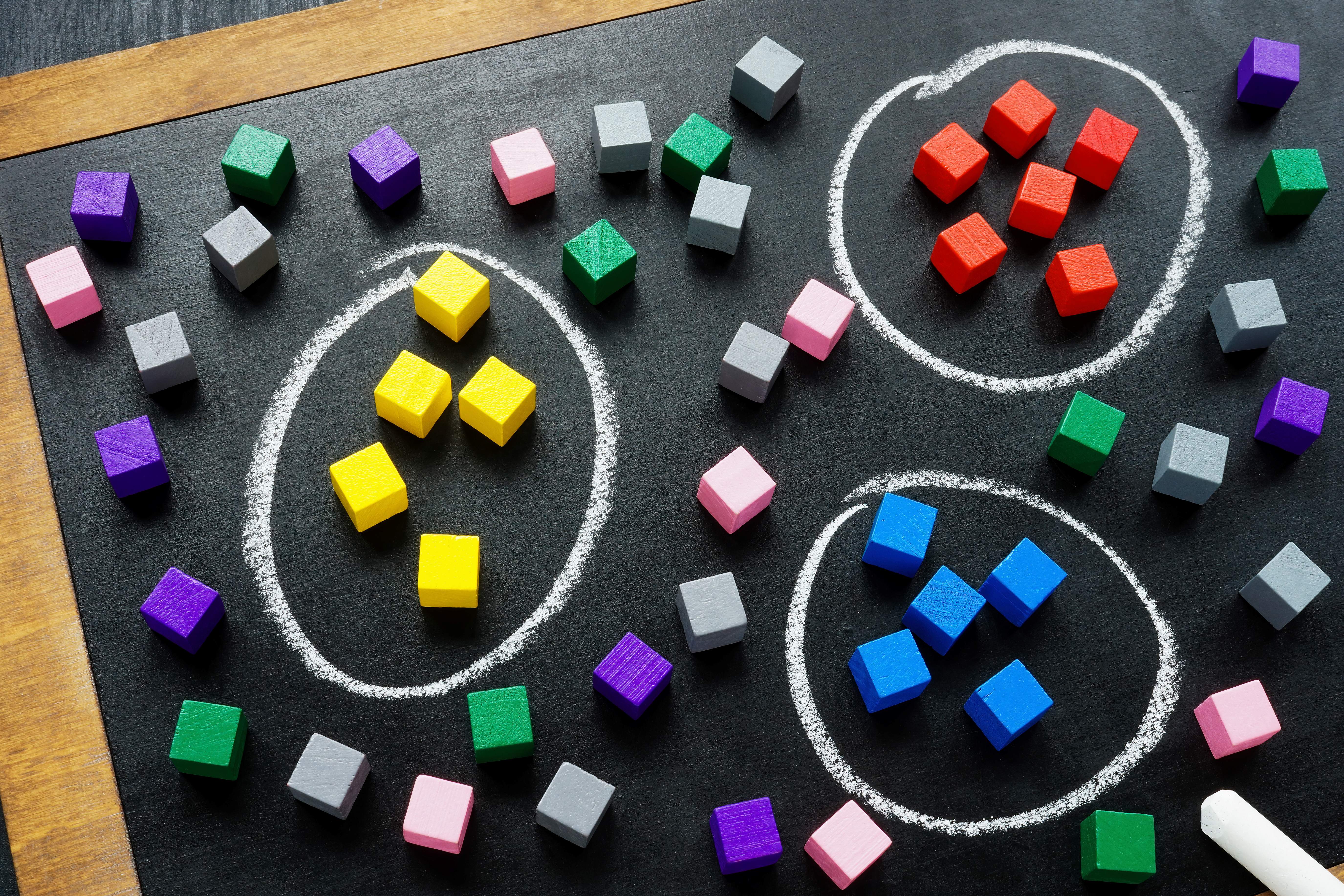 lots of small coloured cubes sit on a blackboard on a desk. Groups of yellow, red and blue cubes are grouped together and circled in chalk.
