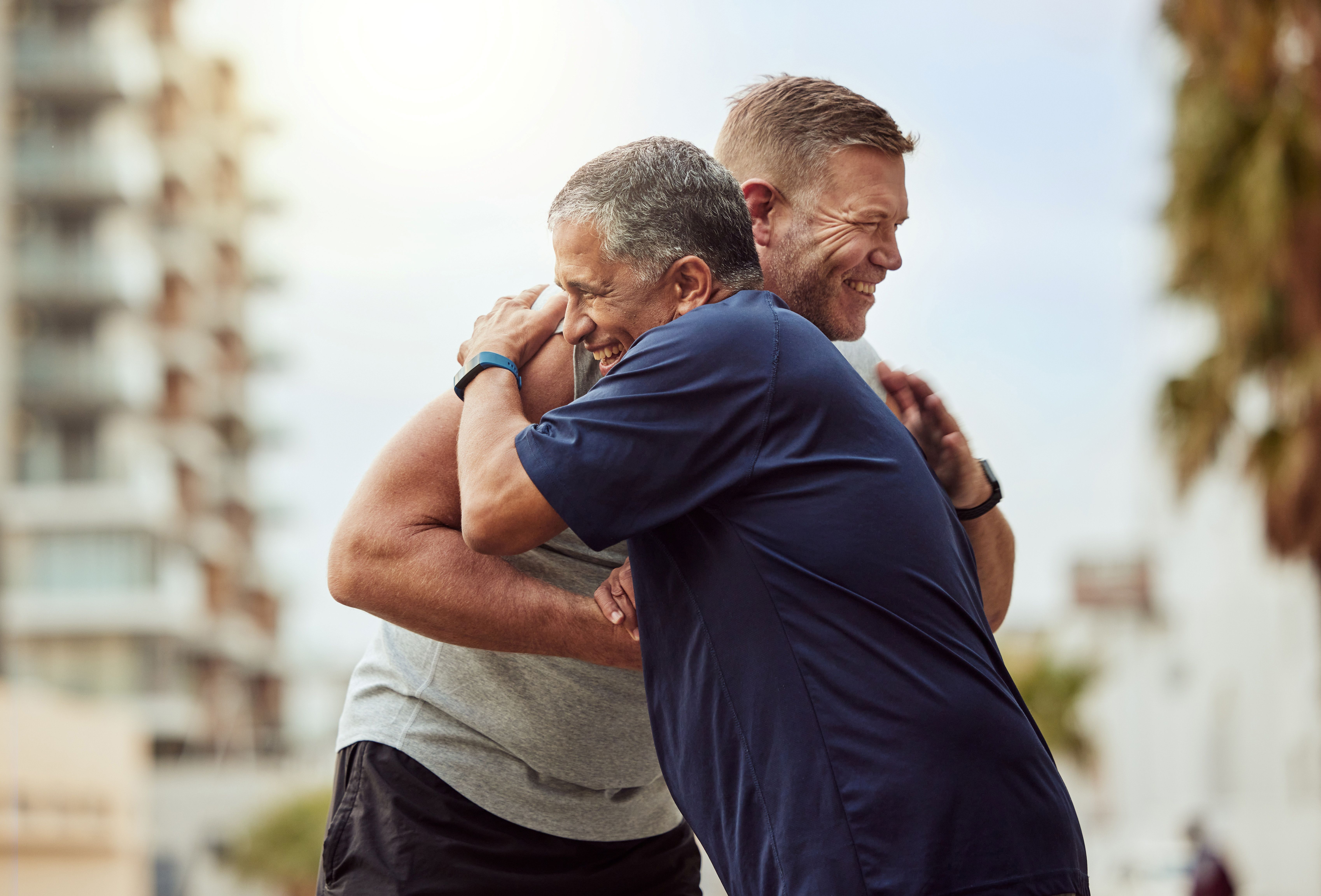 2 smiling guys in t shirts embrace outside