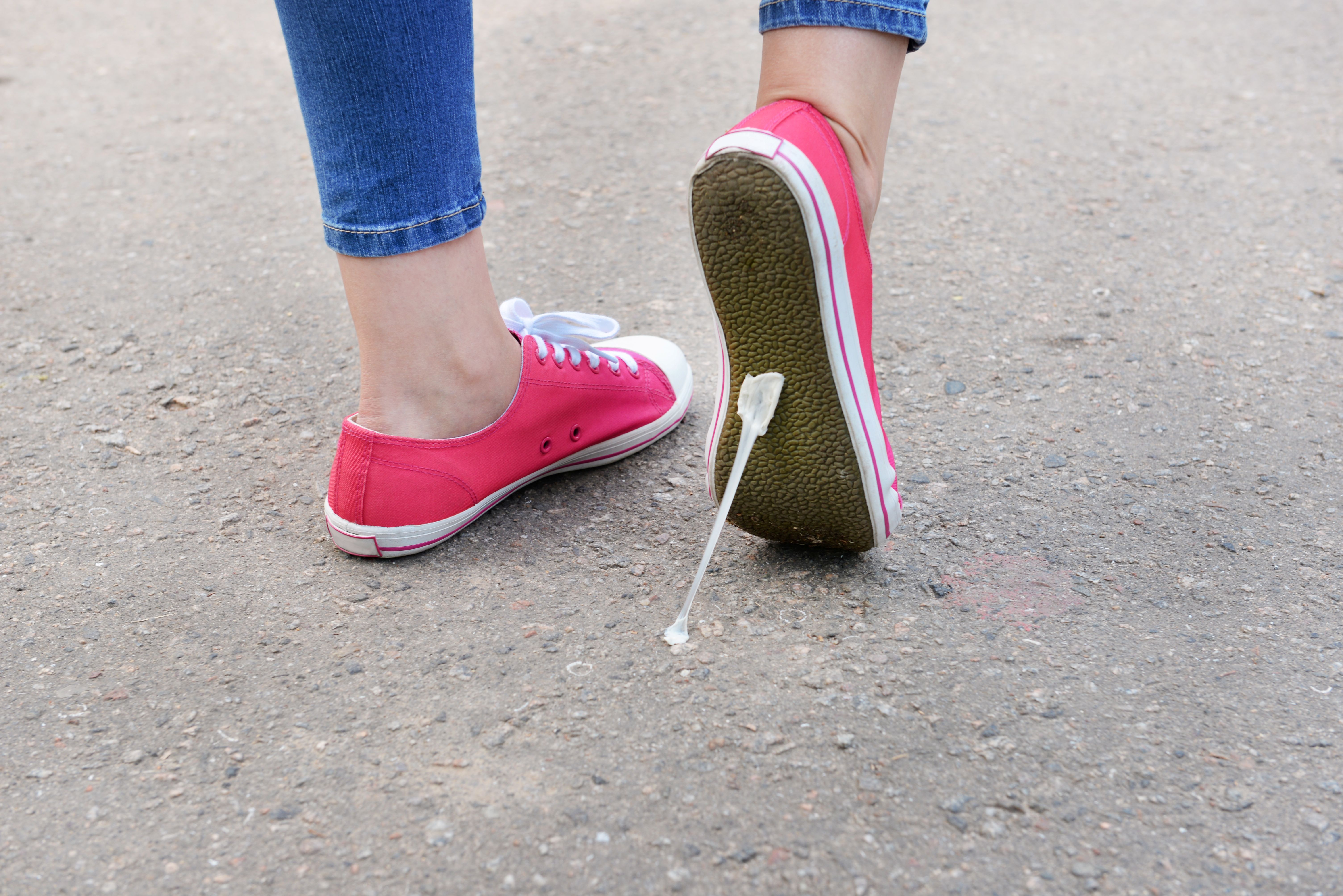 a person's shoe lifting up as they walk and stretching a piece of gum stuck on the floor 