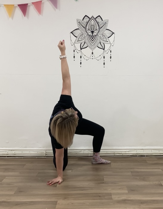 woman kneels on right knee and right hand with left foot on the floor to the left side, knee bent and left hand up to the ceiling.  she looks towards her left hand