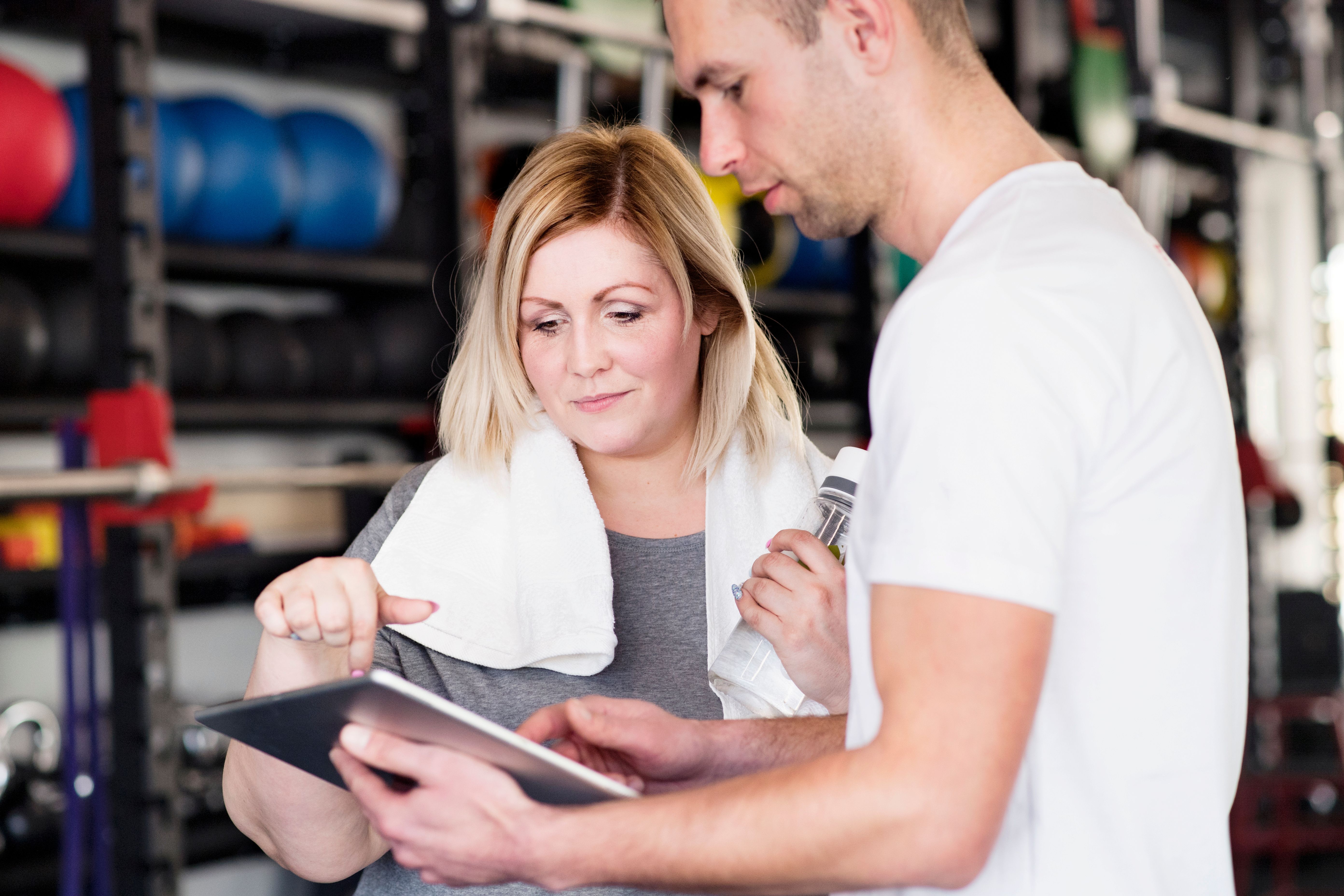 in a gym a male trainer is showing his female client something on his tablet