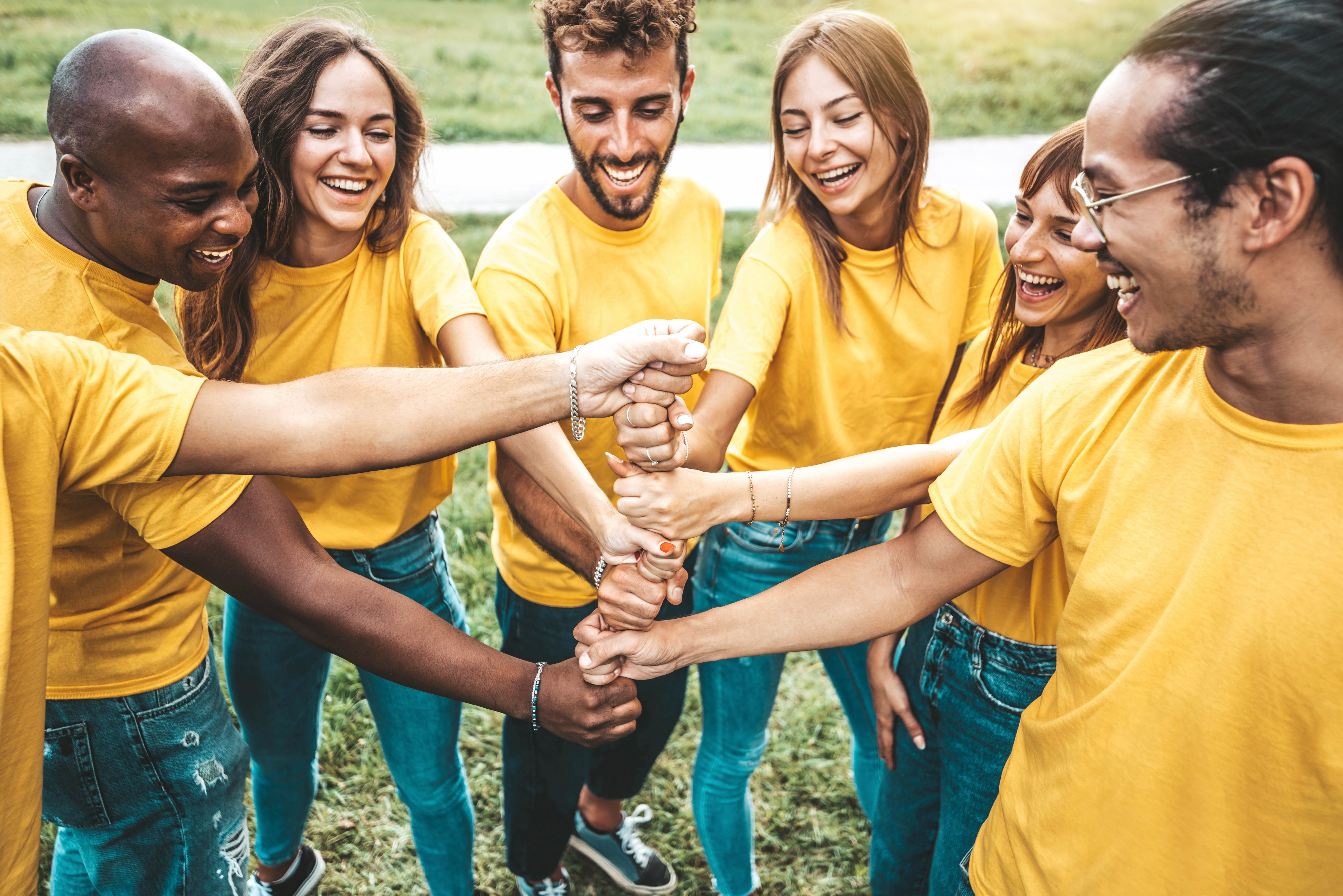 a group of young men and women wearng green jeans and yellow t shirts stack fists in the centre of their circle.