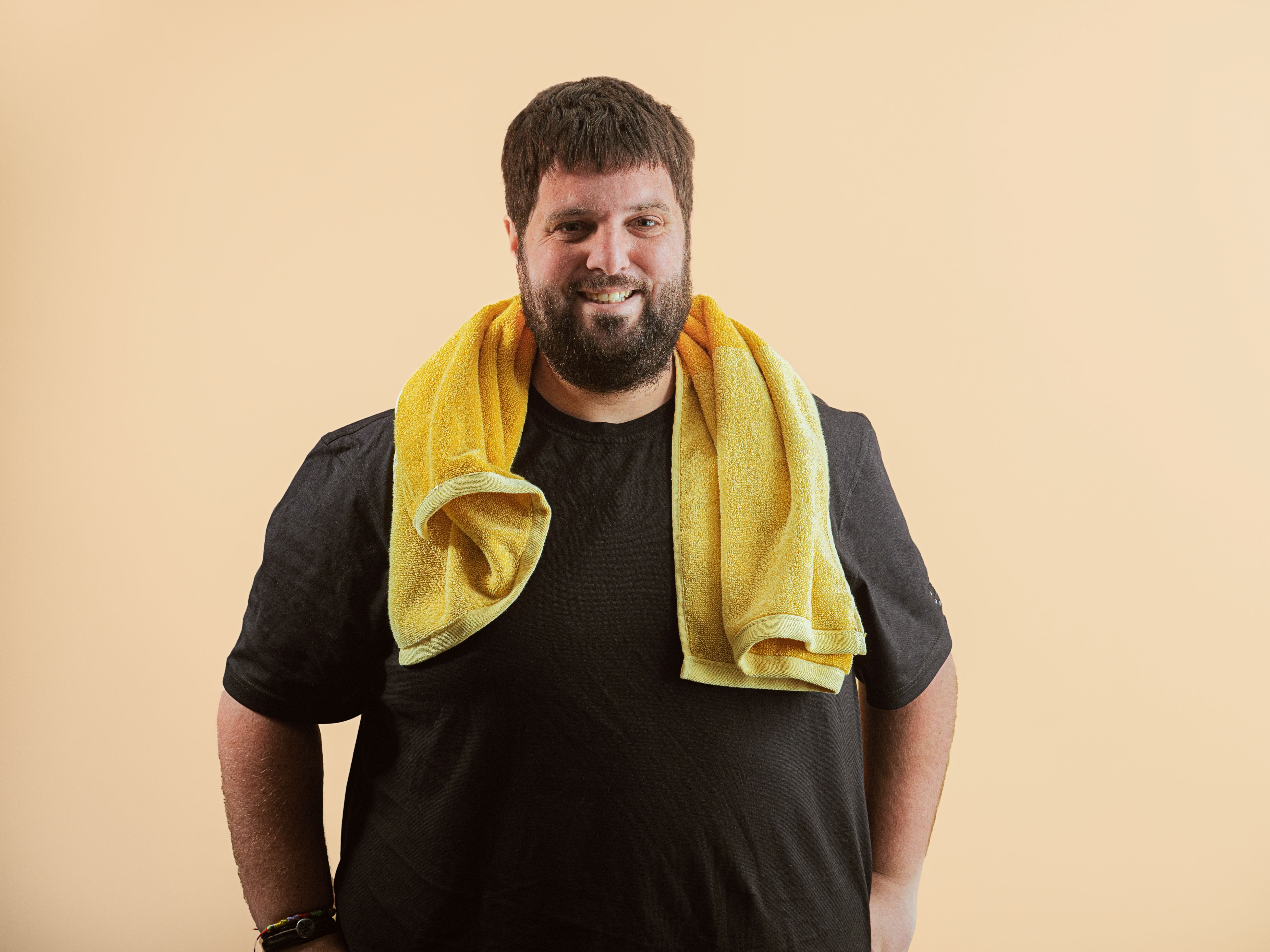 larger young man smiles looking at the camera sweaty after exercising with a towel around his shoulders