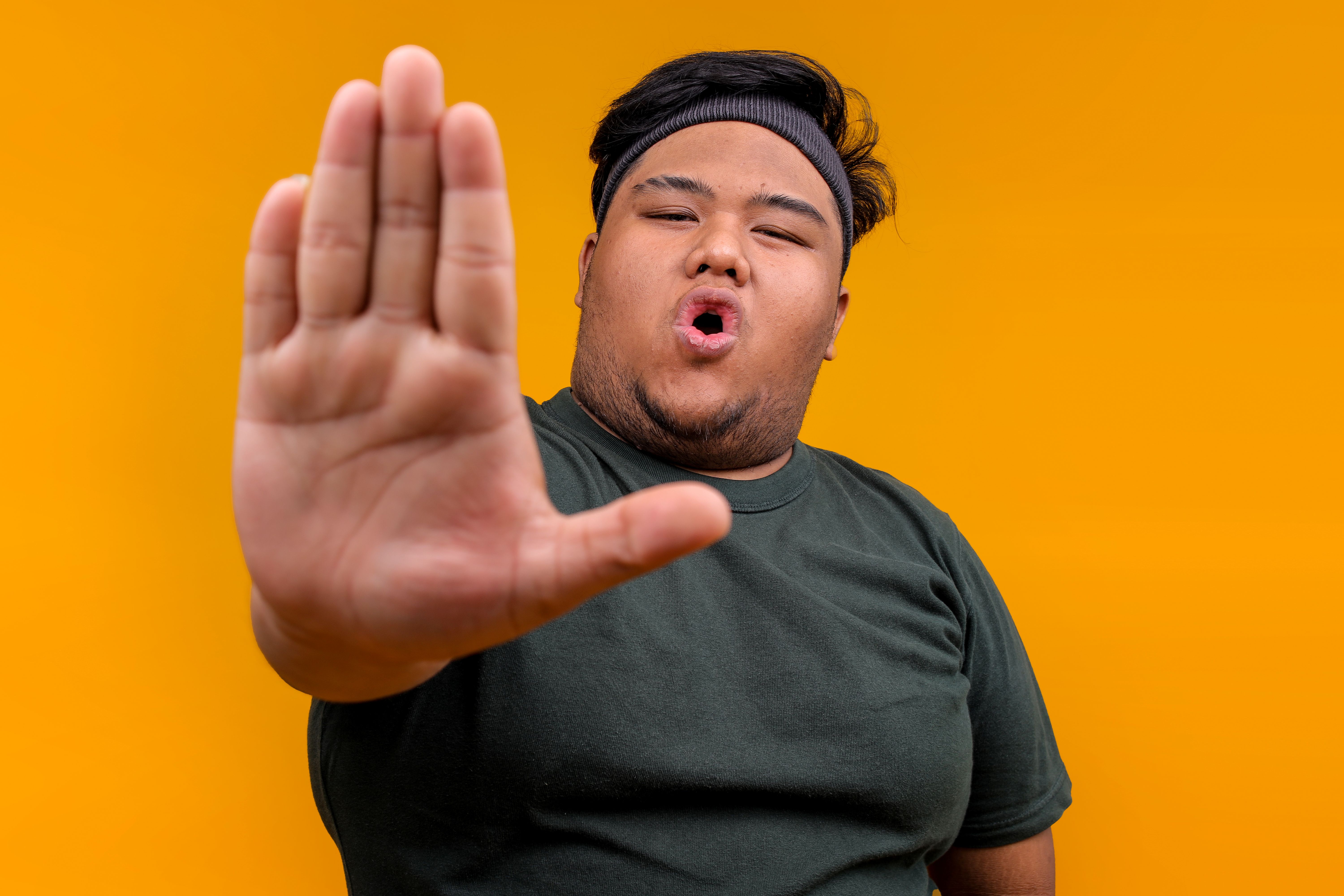 Young Guy in Sportswear Saying No While Showing Palm Hand To Camera Over Yellow Background