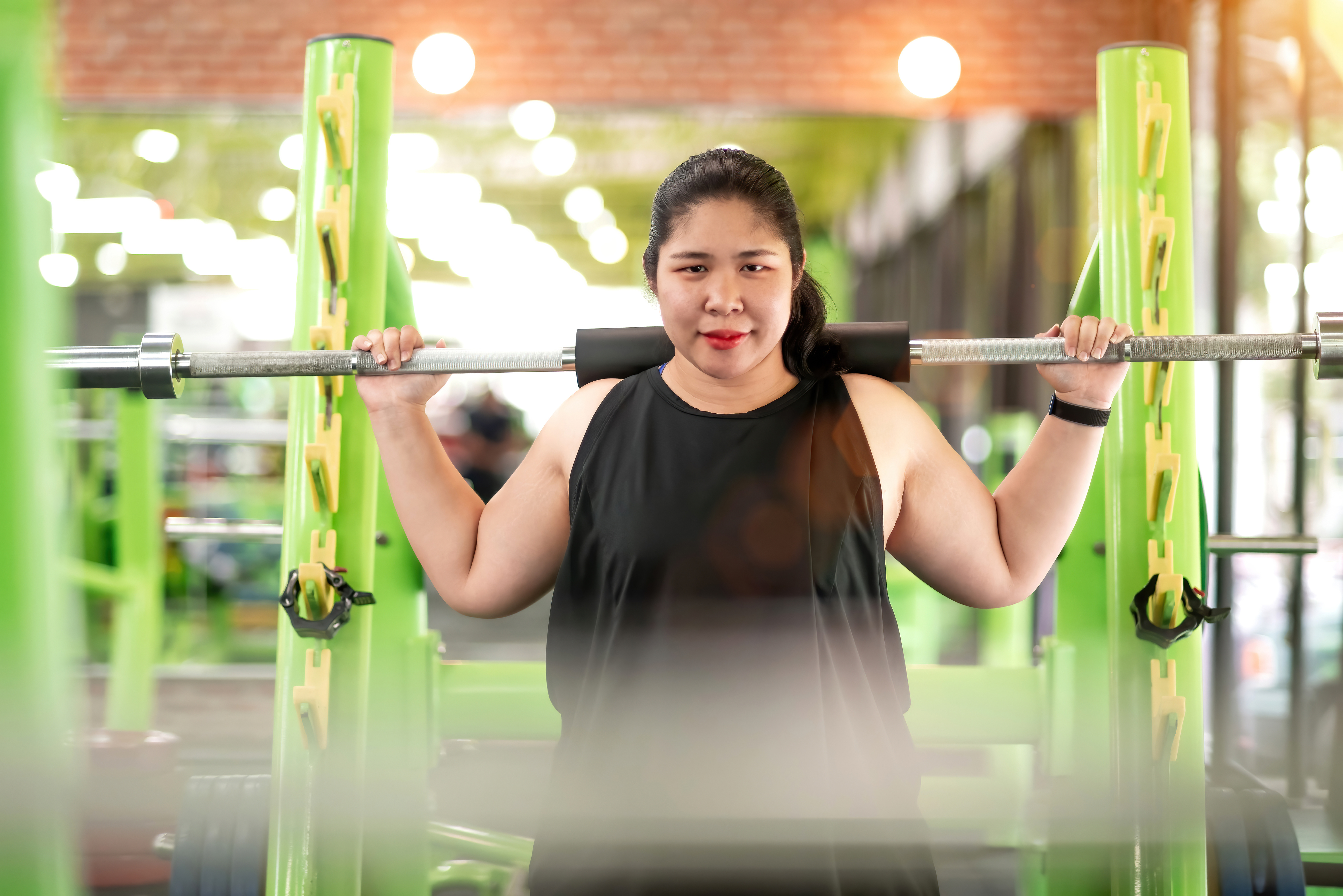 female gym member stands in a rack with a barbell on her shoulders