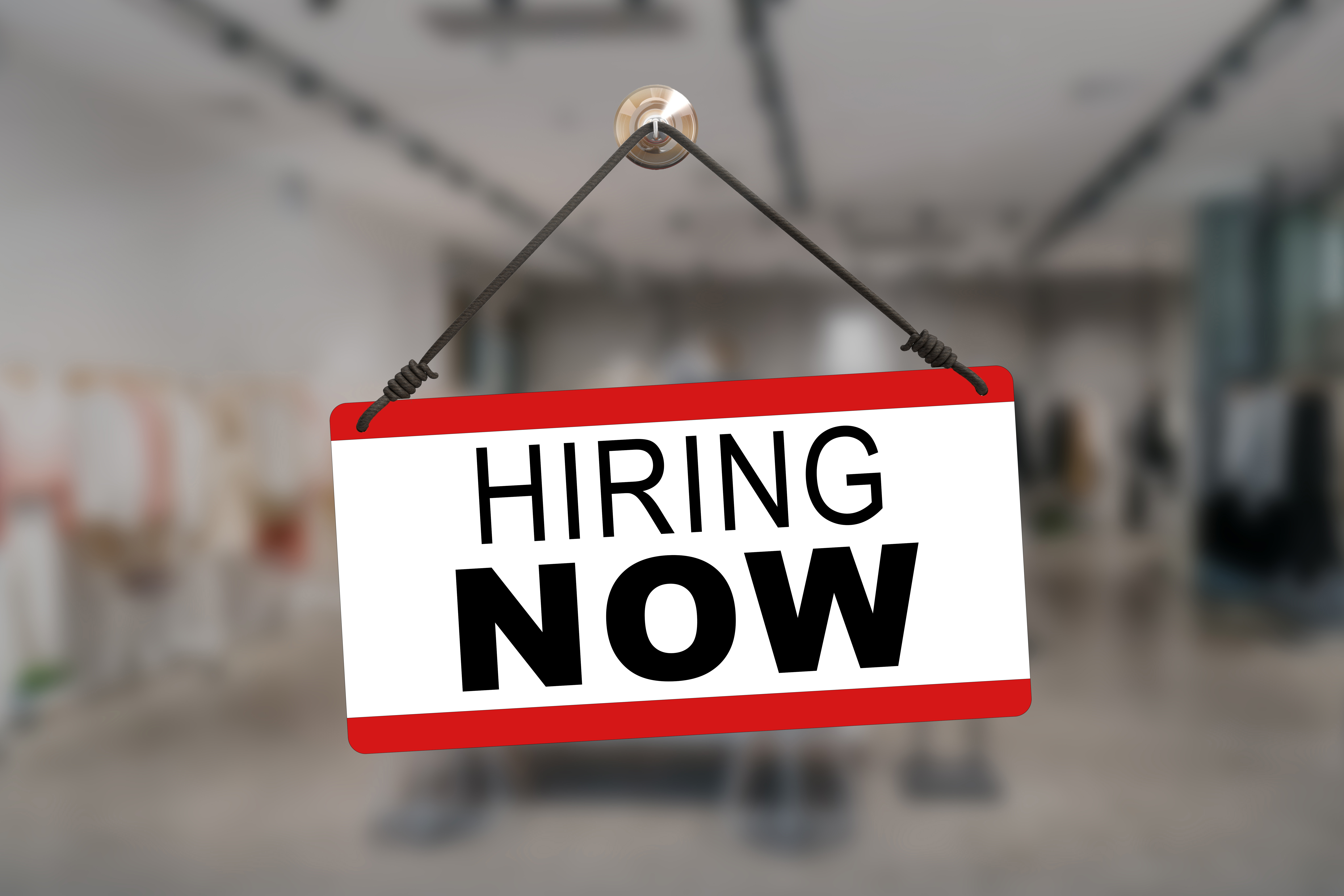 a hiring now sign hangs on a gym door
