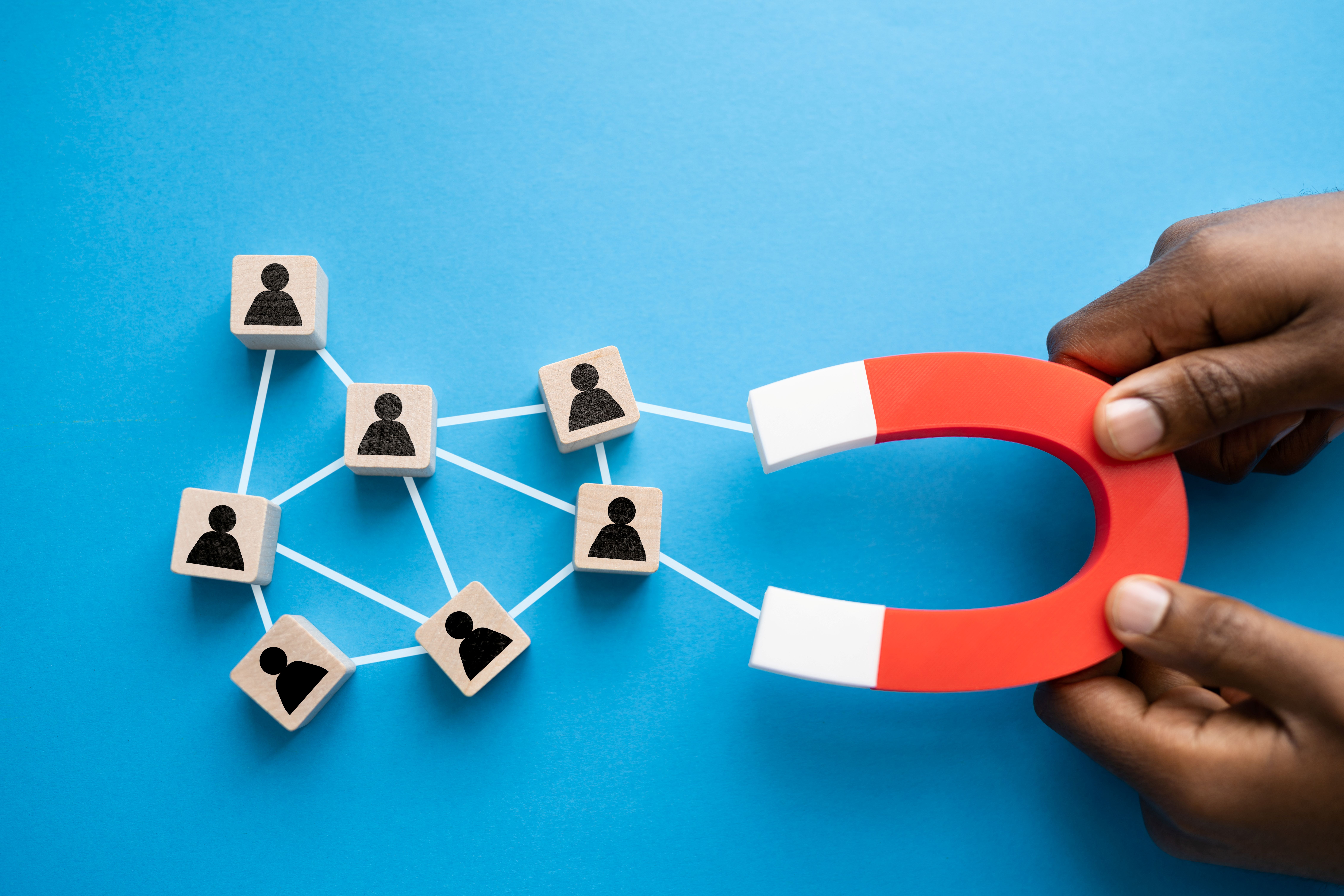 2 hands hold a red and white magnet which is attracting small blocks of wood with people silhouettes on them