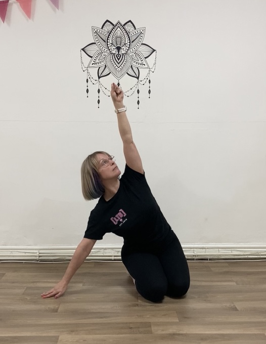 a woman kneels on both knees with right hand on floor beside her and left in the air