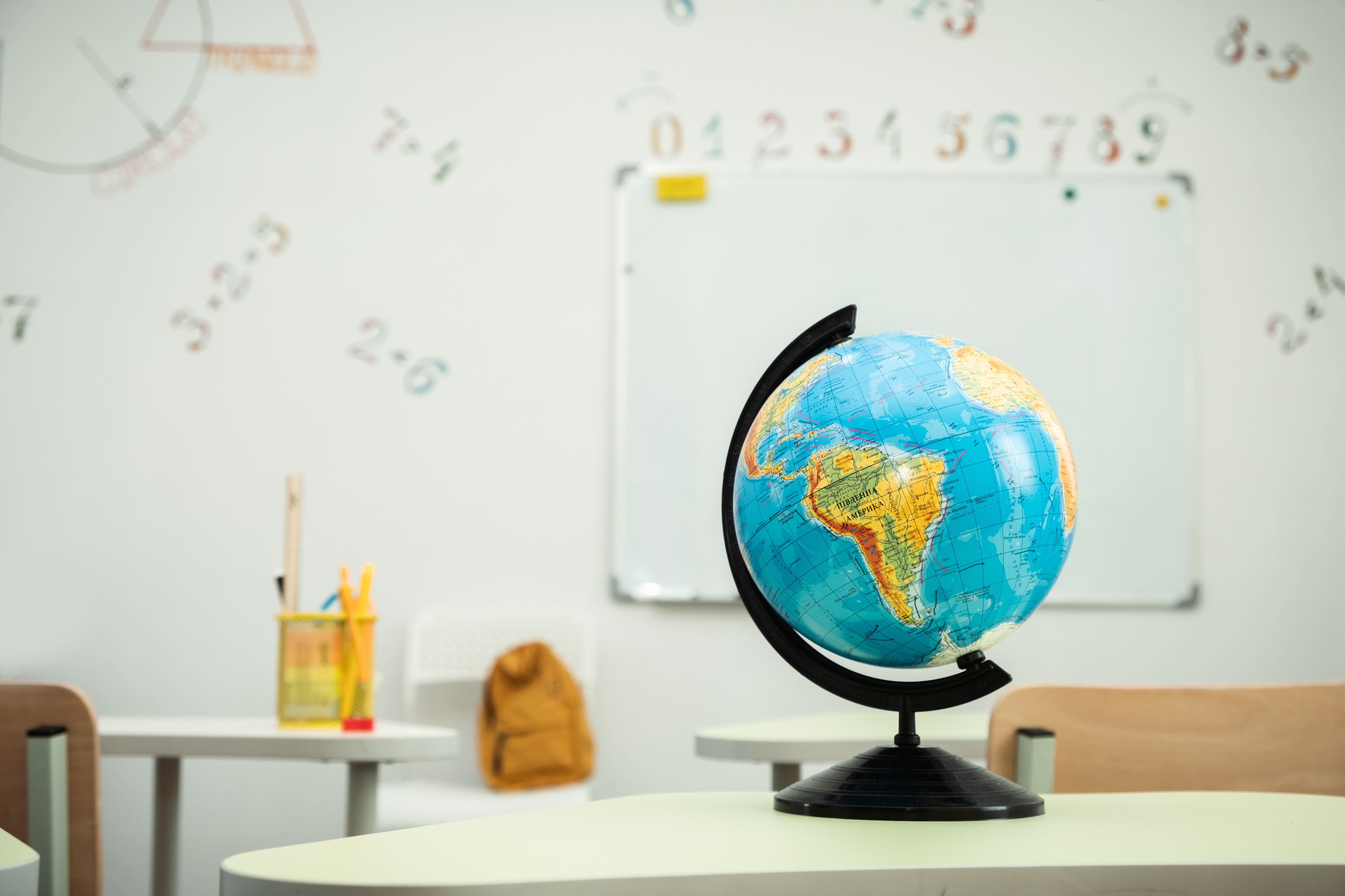 A Globe stands on the desk in the school classroom against the white school board.