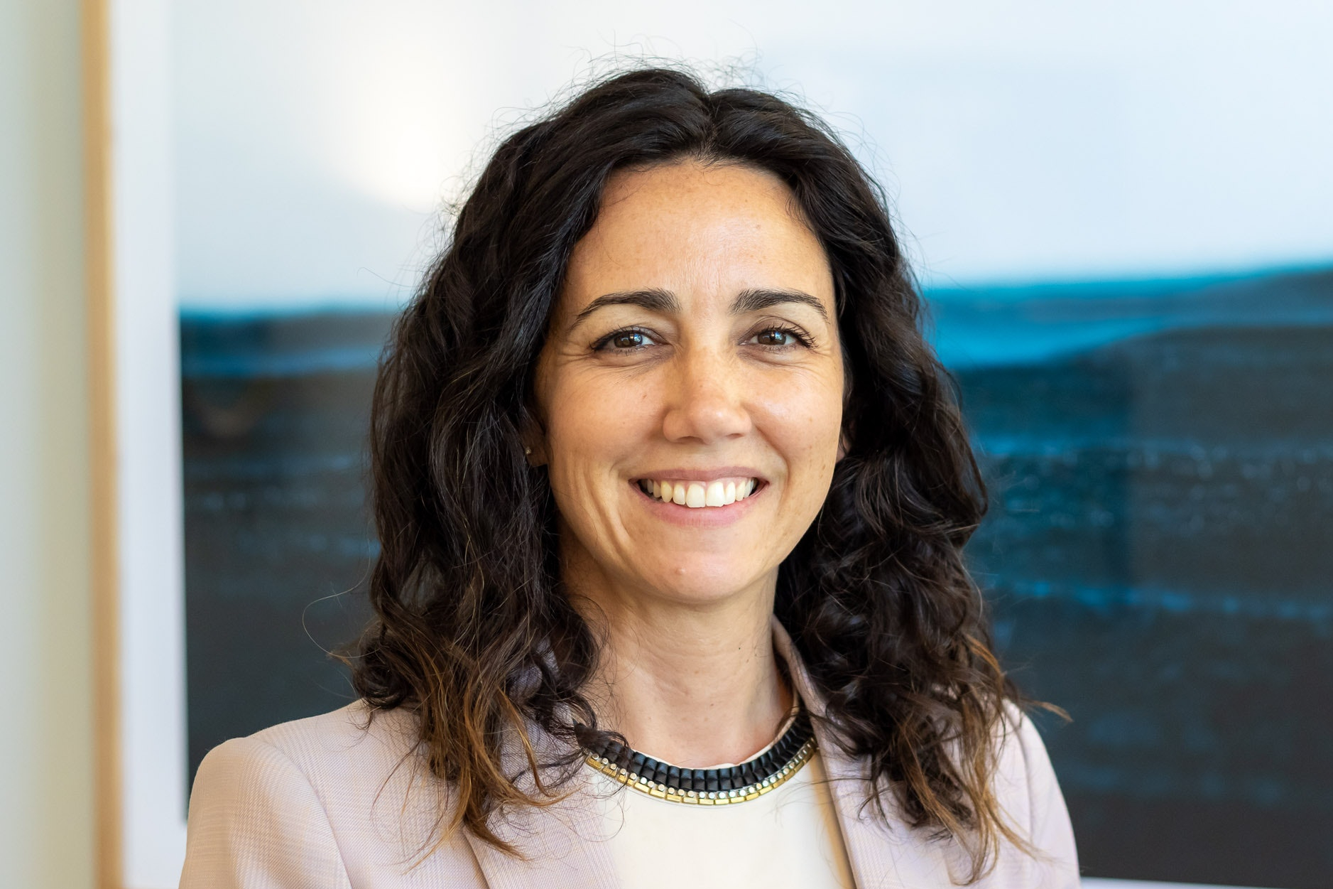 A photograph of Será Godfrey-Kaplan. She is smiling and in the background there is grass and water.