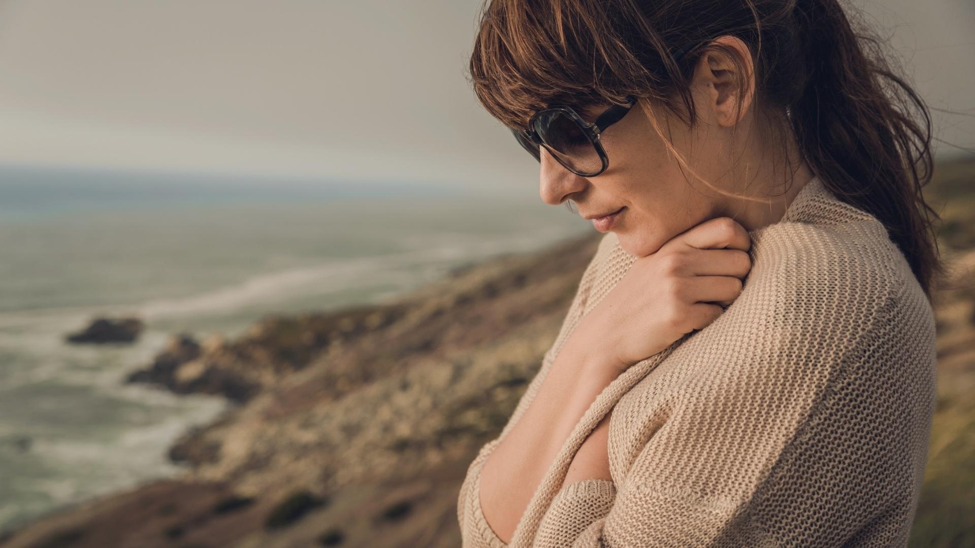 Napszemüvegben a tengerparton gondolkozó nő