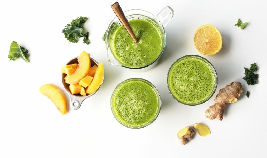 Zöld smoothie poharak felülnézetből, kelkáposztával, gyömbérrel, citrommal és mangószeletekkel