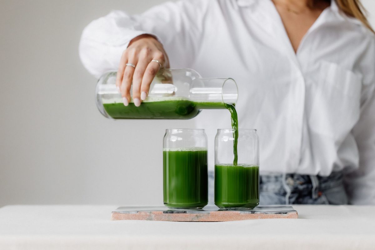 Nő egészséges zöld levet önt üvegkancsóból két pohárba