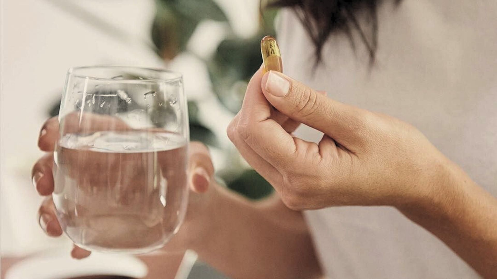 nő kezében egy pohár víz és egy vitamin kapszula