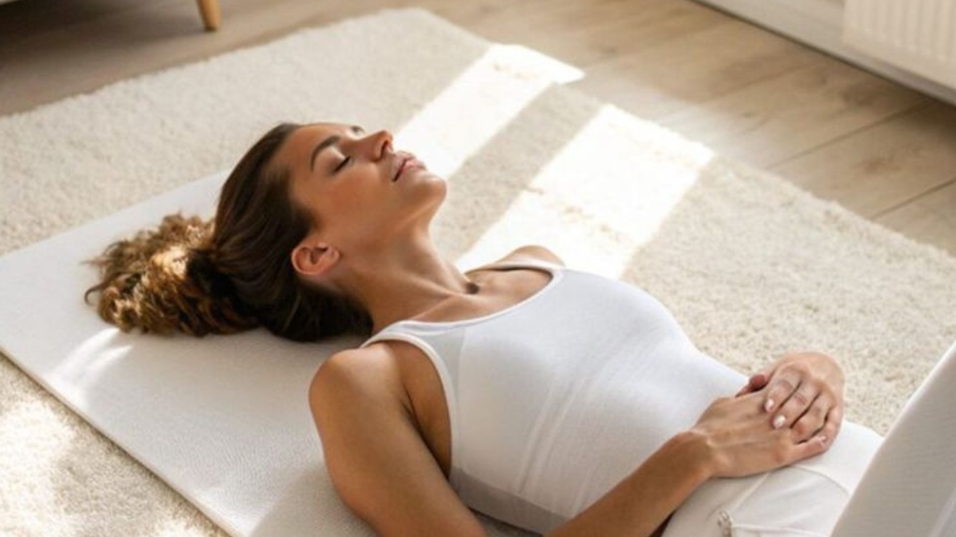 Nő fekszik a szőnyegen és becsukott szemmel meditál