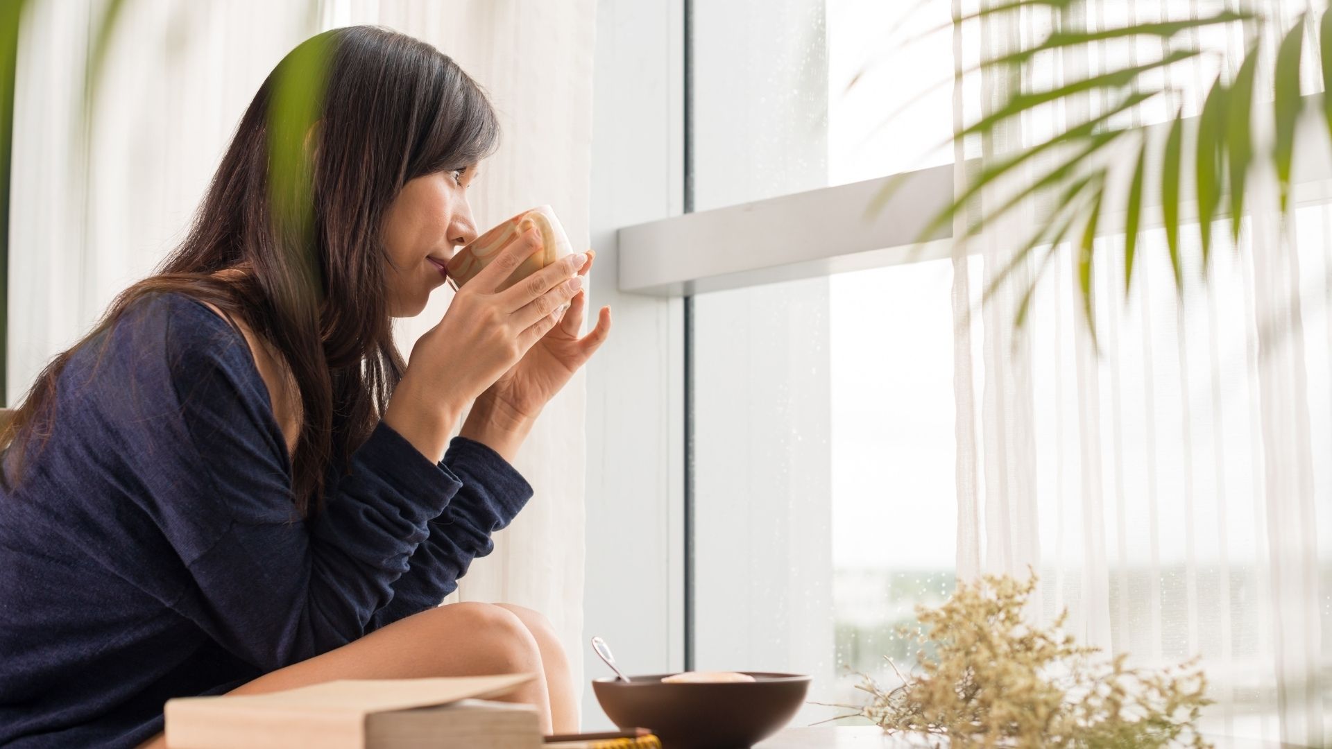 teát kortyolgató boldog nő néz kifelé az ablakon